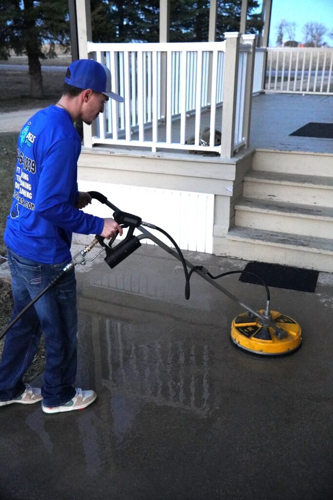 Technician pressure washing a concrete porch with a surface cleaner